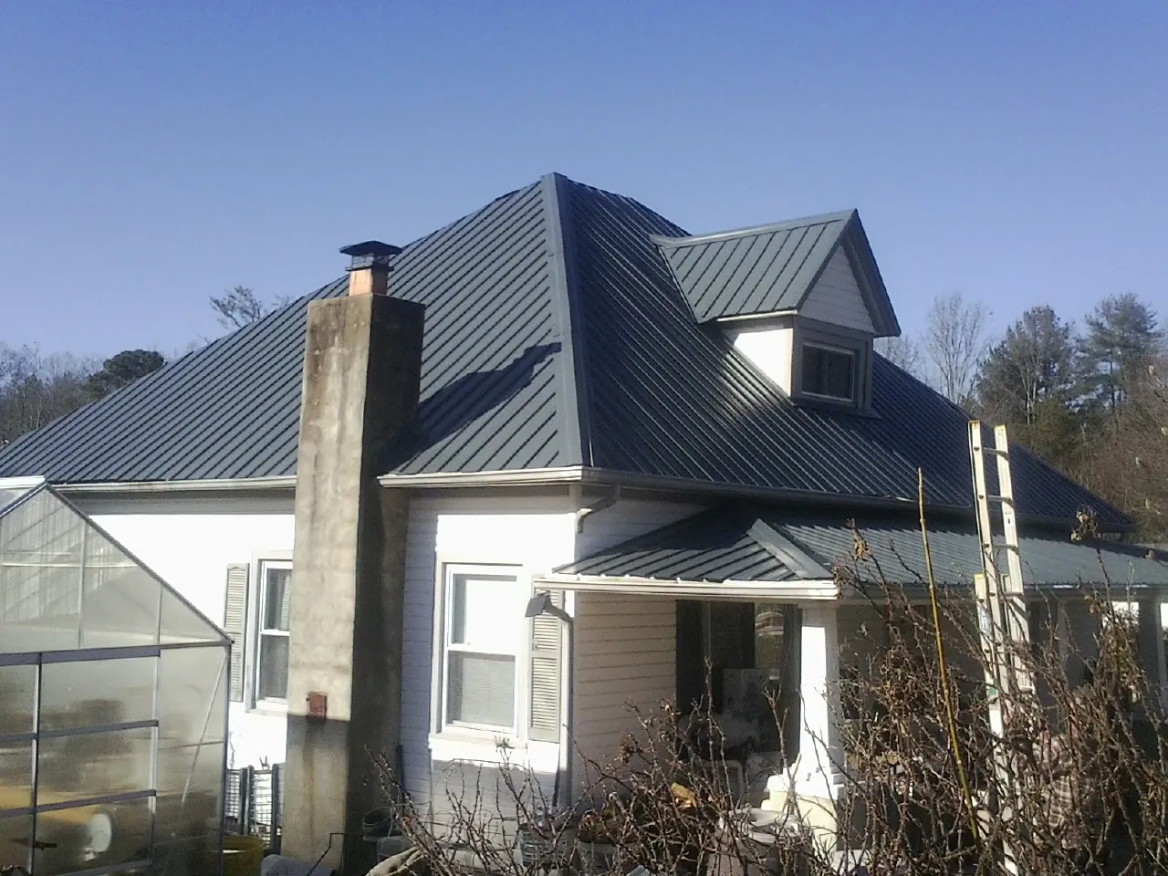 Dark blue standing seam metal roof on a white farmhouse with dormer — Slate & Tile Roof Repair by Roofing Brothers in Prince George