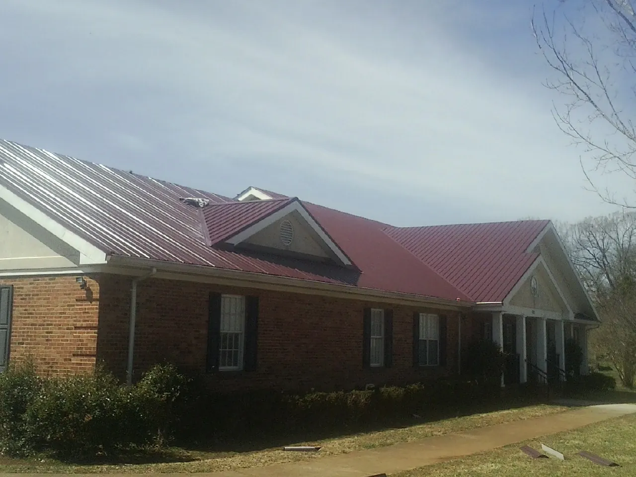 Red metal roof with gabled entries on a long brick building, from a Hail Damage Roof Repair job in Prince George