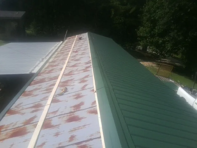 Old rusted panels beside newly installed green metal roofing — Wind Damage Roof Repair by Roofing Brothers in Prince George