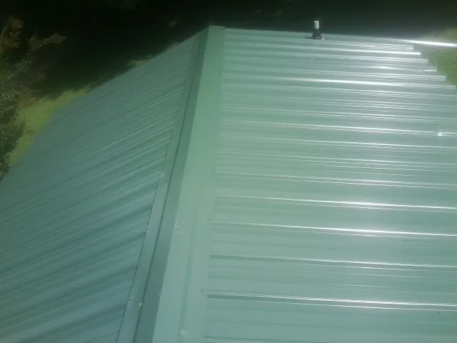 New green metal panels meeting at the ridge of a roof — Flat Roof Repair work by our crew in Prince George