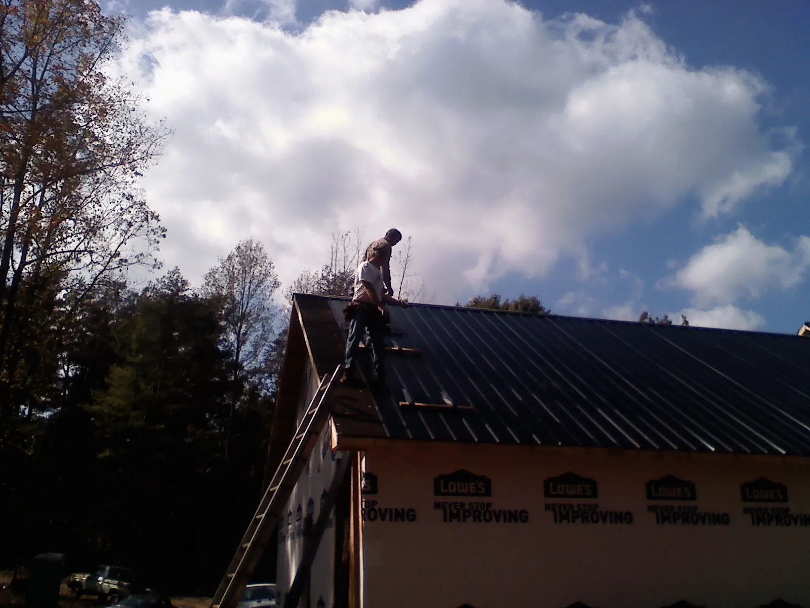 Roofer fastening dark metal panels high against a cloudy sky, from a Roof Inspection job in Prince George