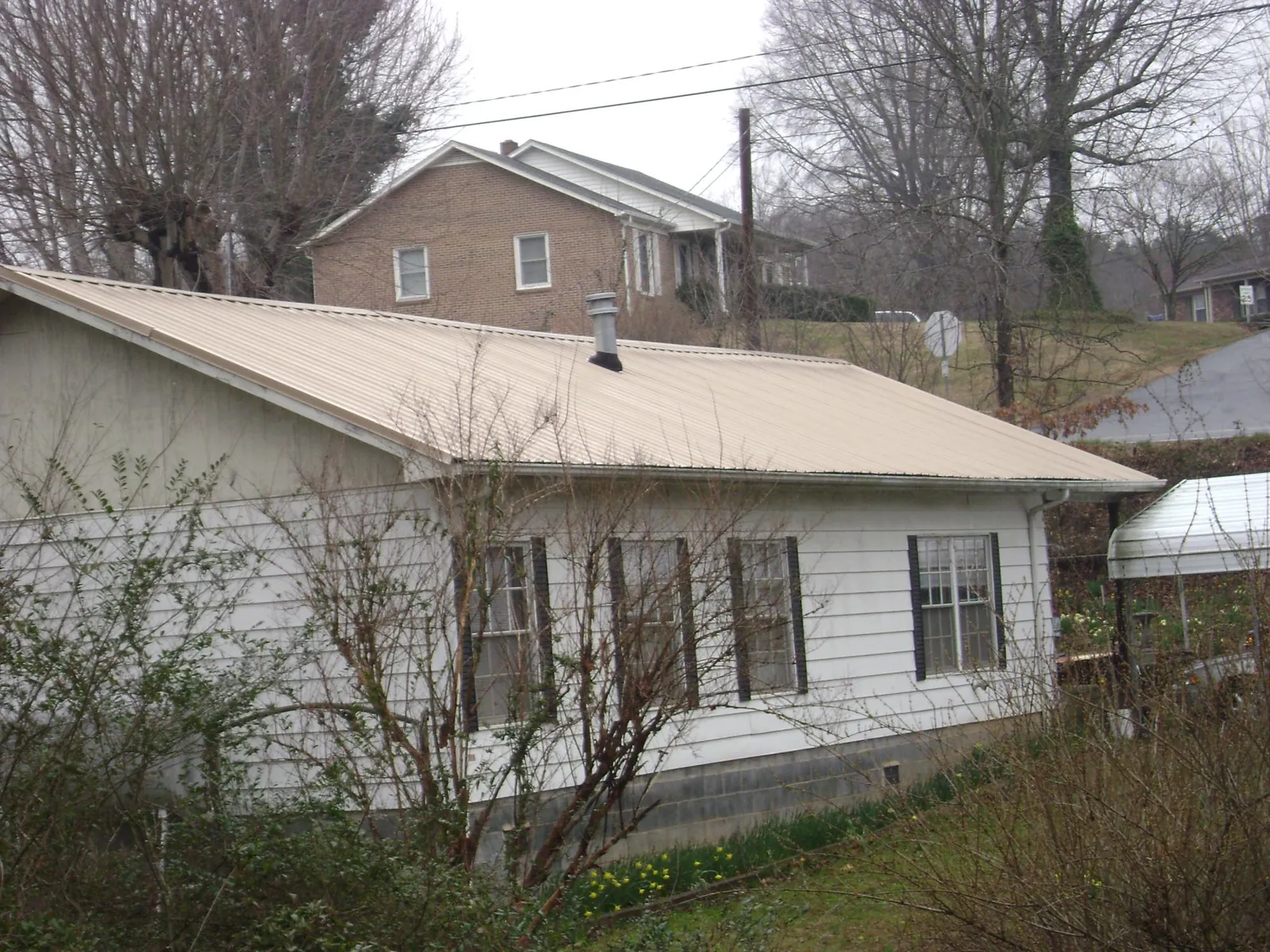 Tan metal roof on a white sided house set into a hillside — Commercial Roofing by Roofing Brothers in Prince George