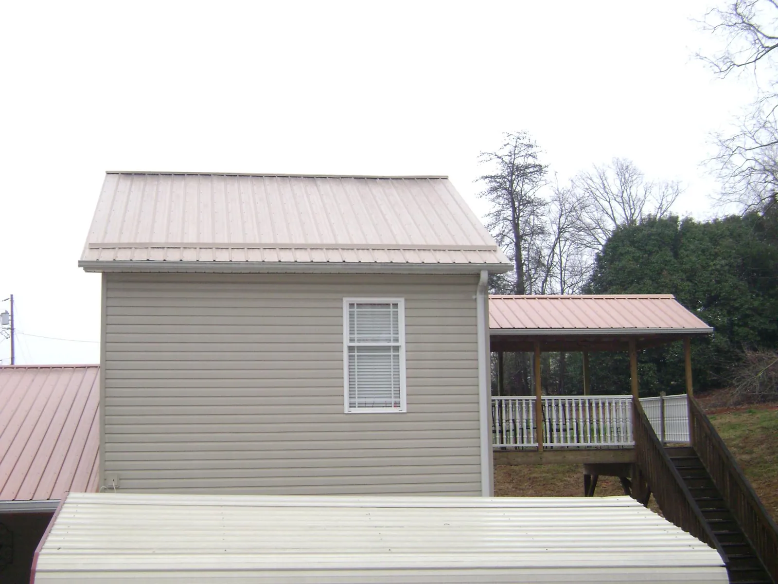 Tan metal roofs on a two story addition and attached porch, from a Roof Replacement job in Prince George